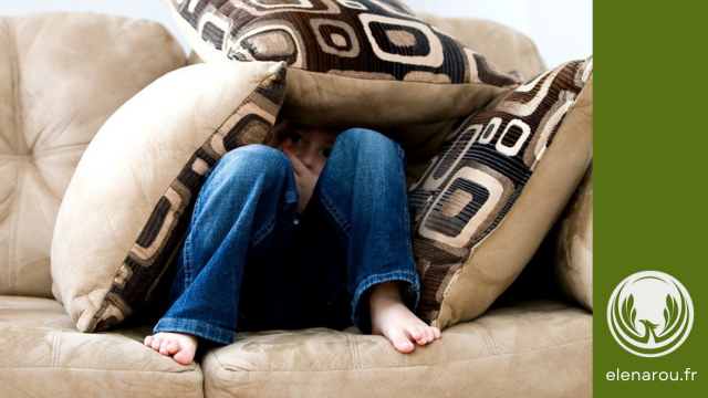 un garçon, qui se cache entre les coussins et qui a peur