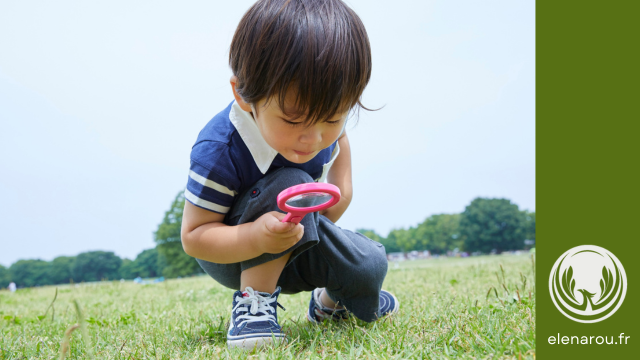 une enfant cherche dans l'herbe avec une loupe