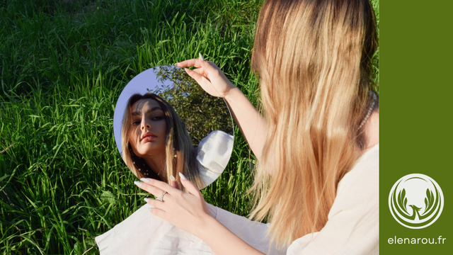 une femme assise sur l'herbe se regarde dans le miroir